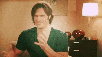 a man in a black shirt is sitting on a couch with his eyes closed and clapping .