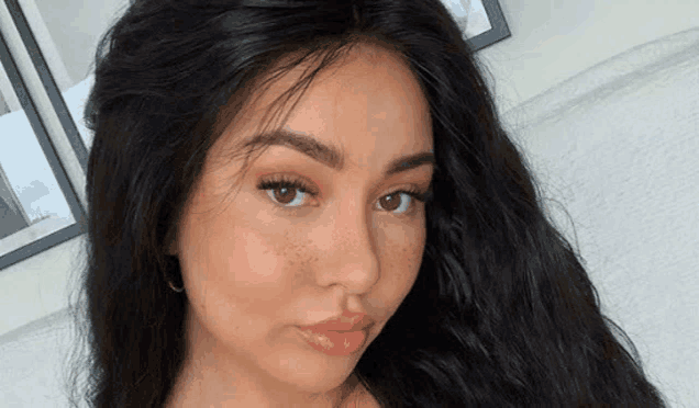 a woman with long black hair and freckles is looking at the camera .