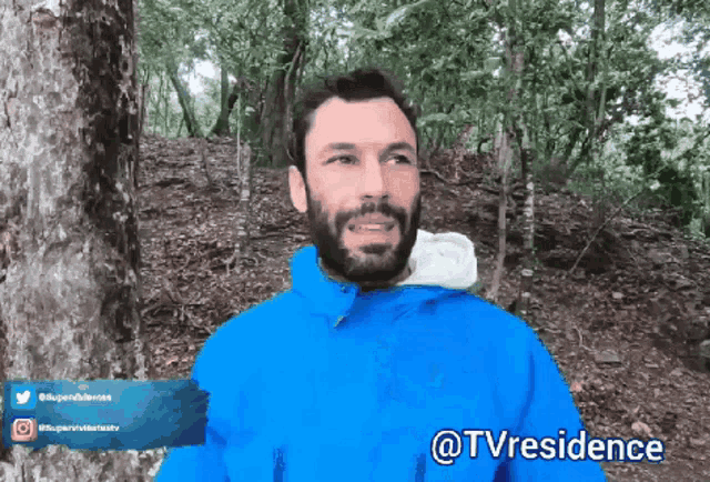 a man in a blue jacket is standing in the woods with the words @tvresidence written below him