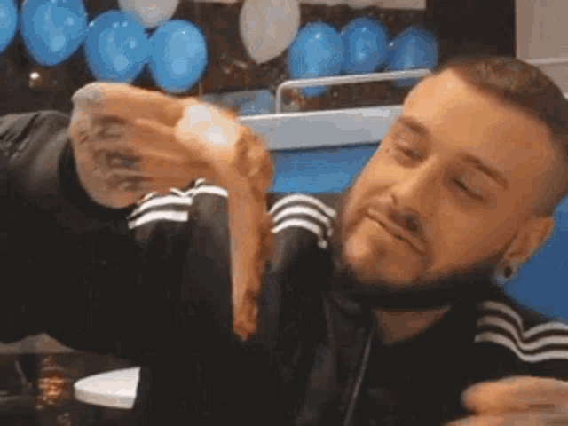 a man with a beard is eating a sandwich in front of balloons .