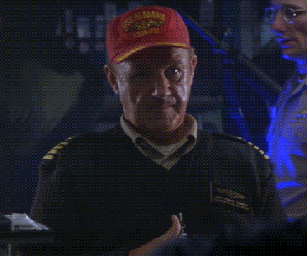 a man wearing a red uss alabama hat giving the peace sign