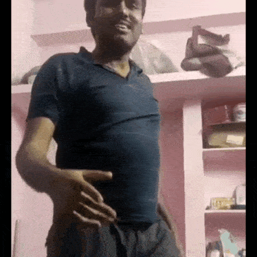 a man in a blue shirt is standing in a room with his hands on his hips and smiling .