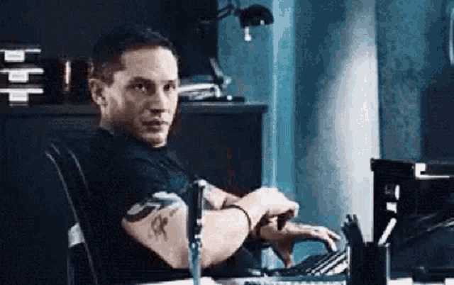 a man is sitting at a desk typing on a laptop .