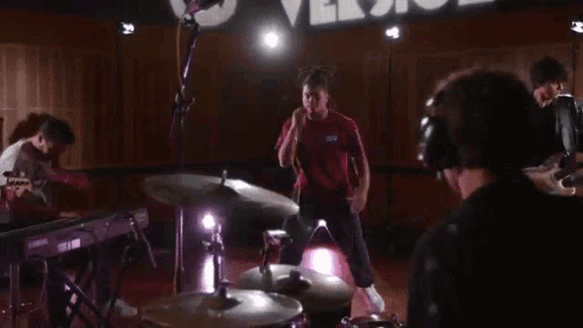 a man in a red shirt is singing into a microphone while playing drums