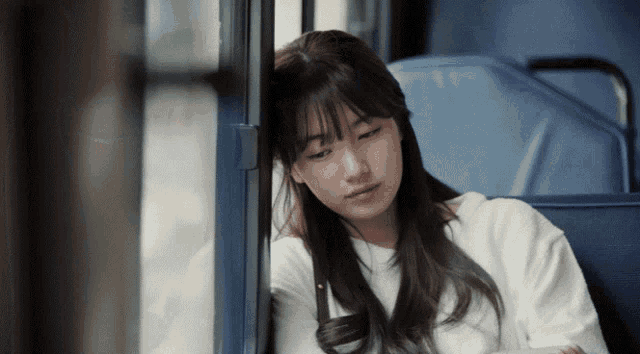a woman sitting on a bus with her head resting on the window