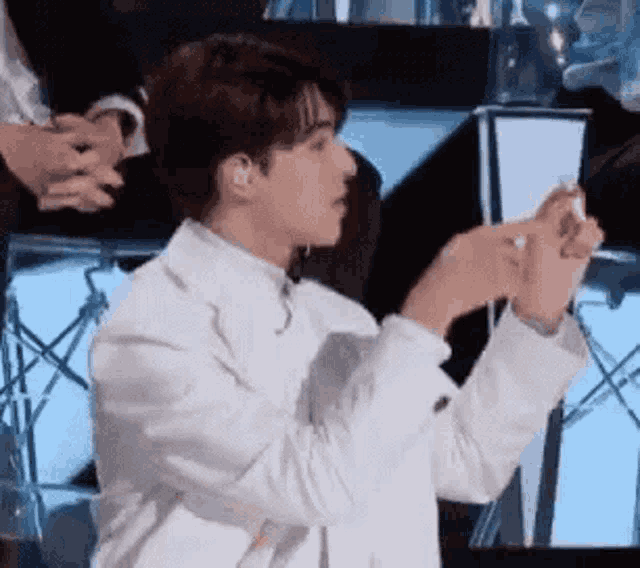 a man in a white suit is taking a picture of himself on a cell phone .