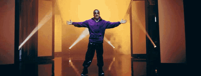 a man in a purple hoodie is standing with his arms outstretched in a hallway