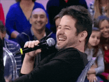 a man is laughing while holding a microphone in front of a crowd of people