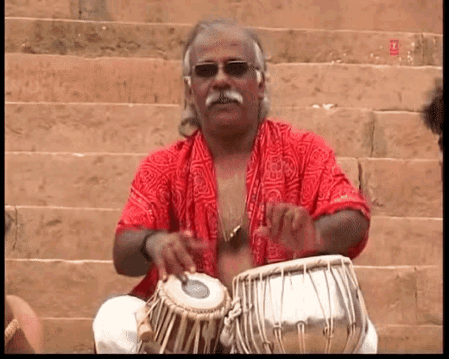 a man in a red shirt is playing drums on stairs