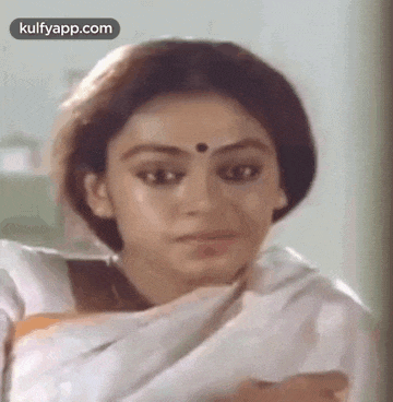 a woman with a bindi on her forehead is wearing a white saree and making a funny face .