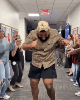 a man in a hat is dancing in a hallway with a group of people .