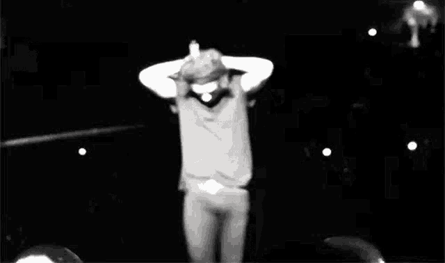 a black and white photo of harry styles dancing on a stage .