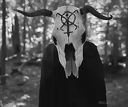 a black and white photo of a person wearing a skull with horns and a cross on it .