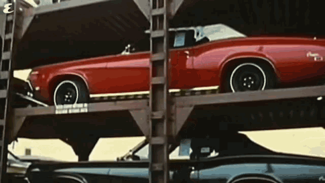 a red car sits on top of a stack of black cars
