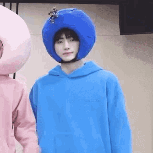 a young man wearing a blue hoodie and a blue hat is standing next to a pink stuffed animal .