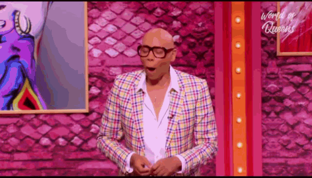 a man wearing glasses and a plaid jacket is standing in front of a pink wall .