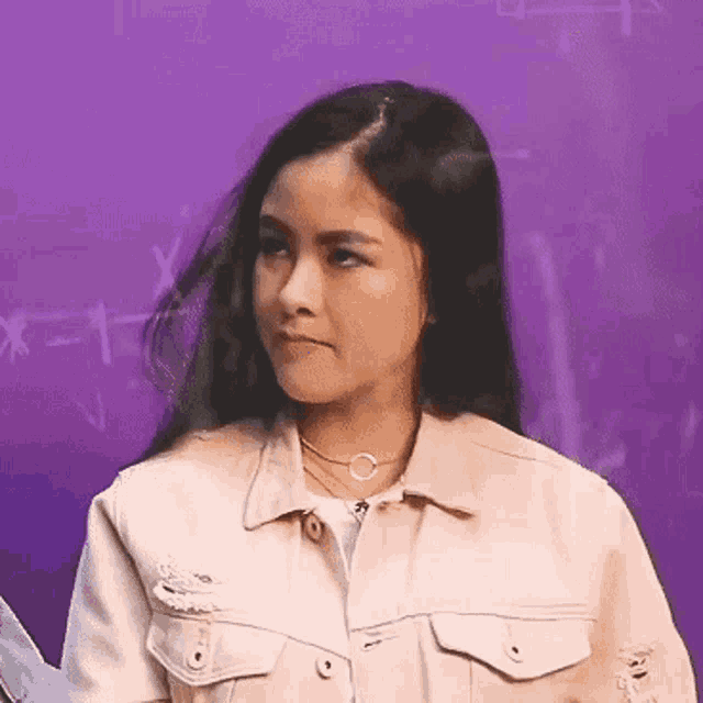 a woman in a white jacket is standing in front of a purple board with a formula on it .
