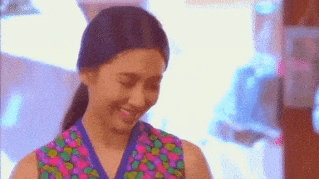 a woman in a colorful floral dress is smiling and looking down .