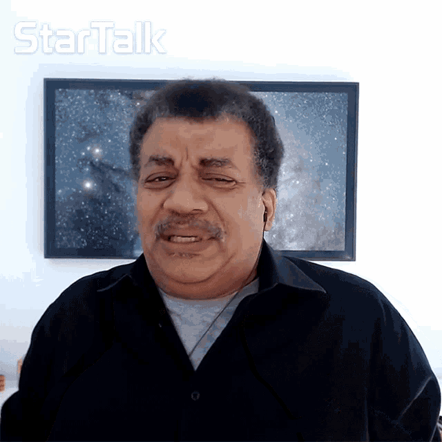 a man wearing ear buds stands in front of a framed picture that says startalk