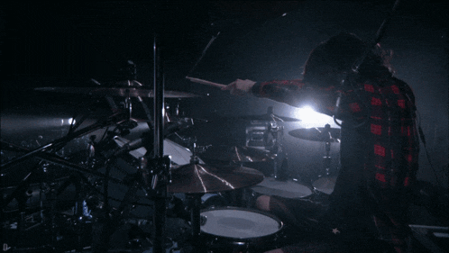 a man in a plaid shirt is playing a drum set