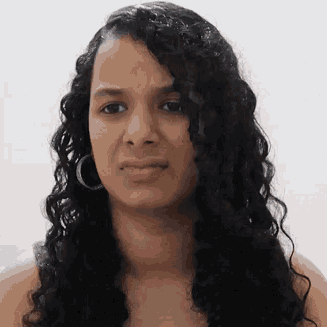 a woman with curly hair and hoop earrings looks at the camera with a serious look on her face