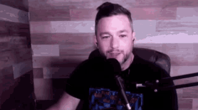 a man with a beard is sitting in front of a microphone .