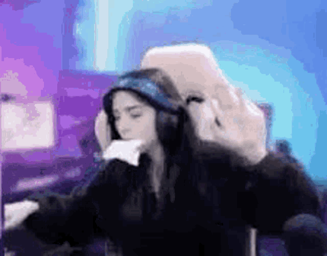 a woman wearing headphones is sitting in front of a computer and holding a cell phone .