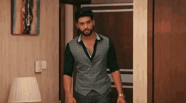 a man in a vest is standing in a room