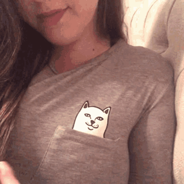 a woman wearing a gray shirt with a cat in the pocket