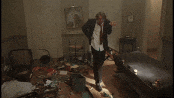 a man in a suit and tie is standing in a messy room with a car in the background .
