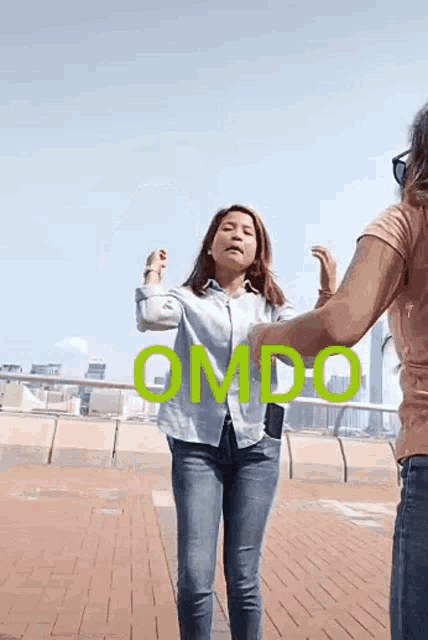 two women are dancing in front of a sign that says " omdo " on it