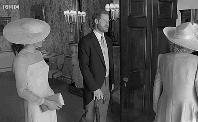 a man in a suit and tie is holding an umbrella while standing next to a woman in a white dress and hat .