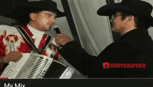 a man in a cowboy hat is talking into a microphone while another man holds an accordion