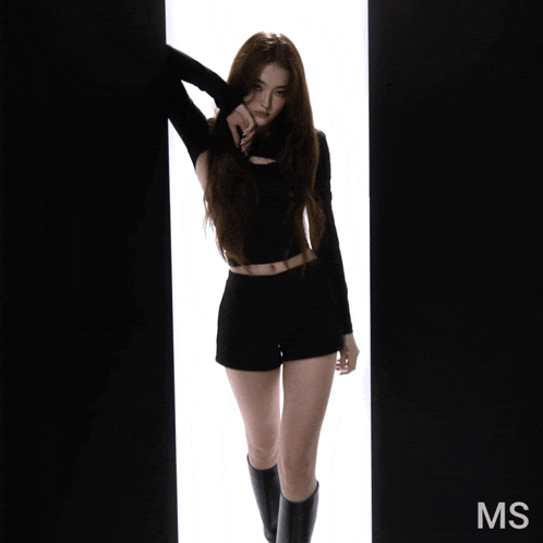 a woman in a black top and shorts is standing in front of a white wall with the word ms on it