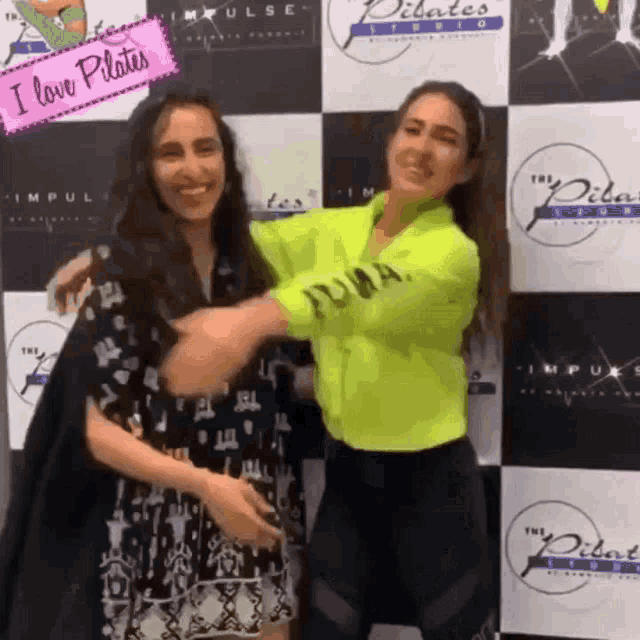 two women hugging in front of a sign that says pilates