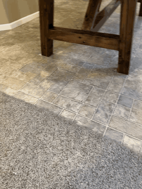 a wooden table sits on a tile floor next to a carpet