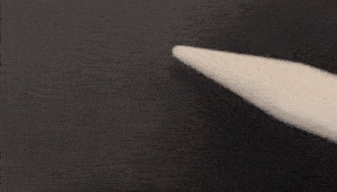 a close up of a white pencil pointing to a black surface .