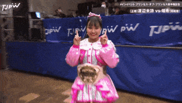 a girl in a pink dress stands in front of a blue tjpw banner