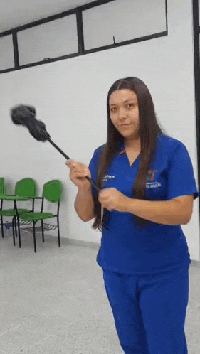 a woman in a blue scrub is holding a mop in her hand .