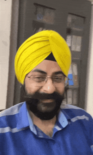 a man wearing glasses and a yellow turban smiles for the camera