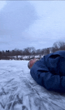 a man in a blue jacket is laying in the snow .