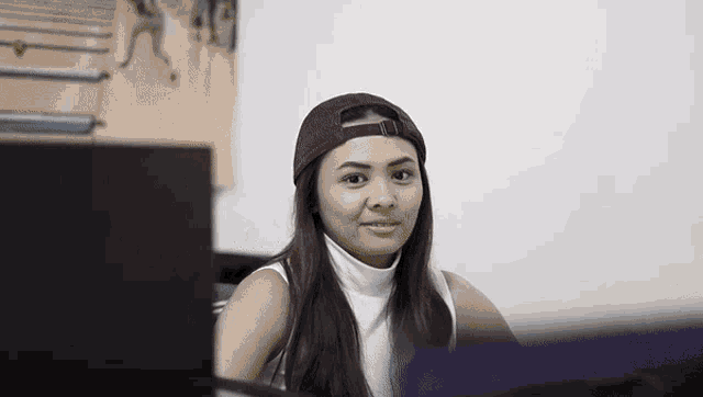 a woman wearing a hat and a white tank top smiles