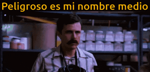 a man with a mustache is standing in front of a shelf with the words peligroso es mi nombre medio above him