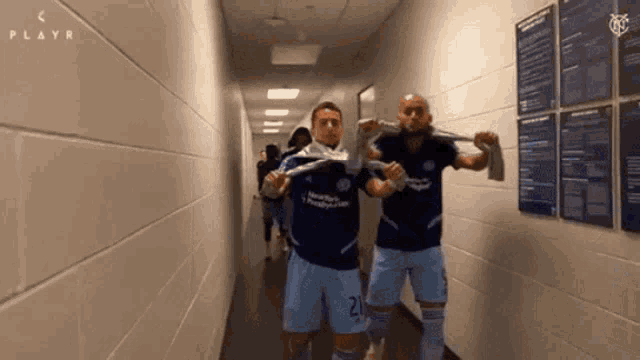 two soccer players in a hallway with a playr logo on the wall behind them
