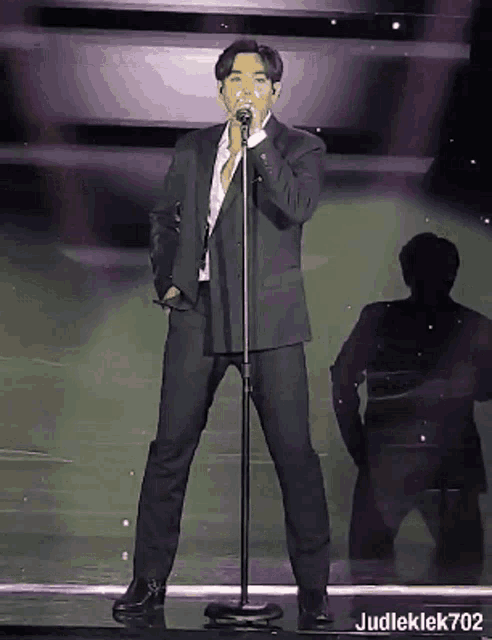 a man in a suit is singing into a microphone with judleklek702 written below him
