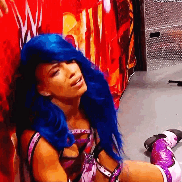 a woman with blue hair is sitting in front of a wall that says wwe