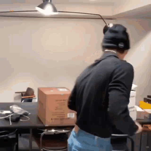 a man in a black jacket and a black hat is standing in a room with boxes on the floor .