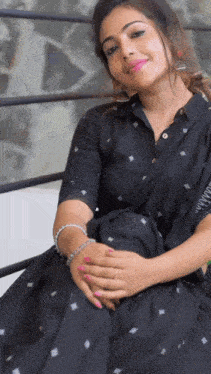 a woman in a black dress is sitting on a bench with her hands folded