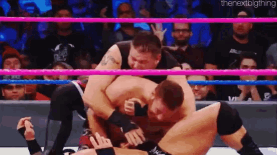 two men are wrestling in a ring with a crowd in the background .
