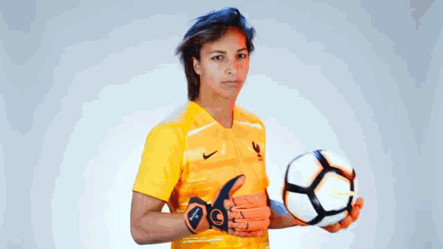 a woman in a yellow shirt and orange gloves is holding a nike soccer ball